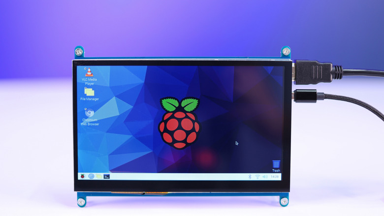 A small, portable monitor displaying the Raspberry Pi OS desktop with the Raspberry Pi logo on the wallpaper.