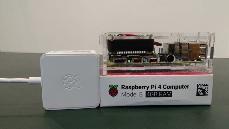 A Raspberry Pi 4 sitting on its box with a transparent case and a power supply next to it.