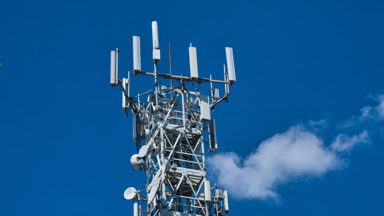 Cellular tower with multiple antennas and dishes against a clear blue sky with a small cloud nearby.