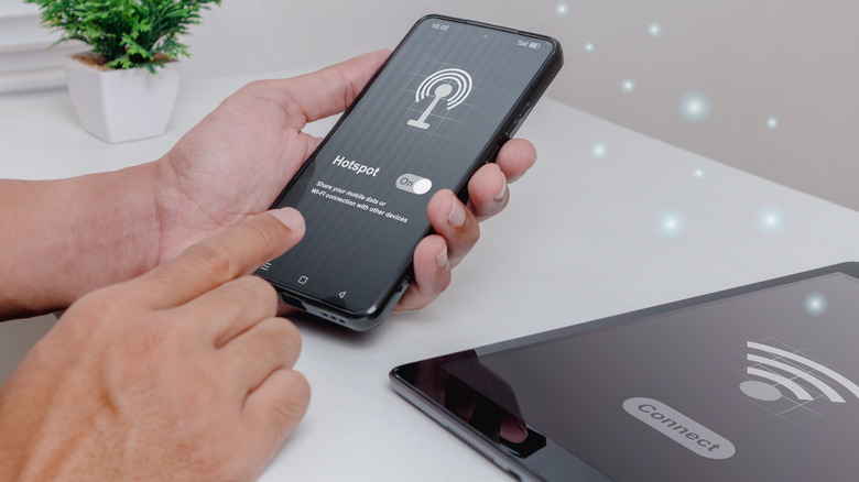 Person turning on a smartphone hotspot feature while another device nearby shows a Wi-Fi connection prompt.