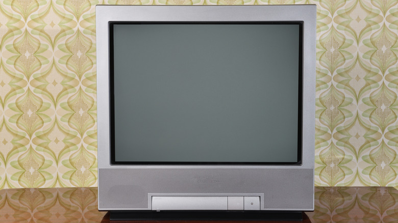 Flat-screen television with a blank screen on a wooden surface, set against retro patterned wallpaper.