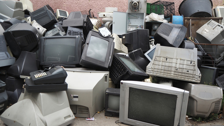 Pile of discarded old CRT televisions and computer monitors stacked outdoors, forming a heap of electronic waste.