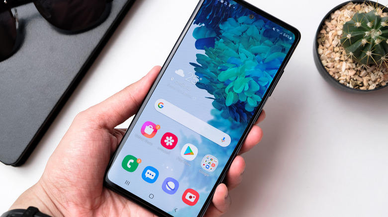 Samsung Galaxy S20 FE 5G phone in someone's hand with office workspace background.