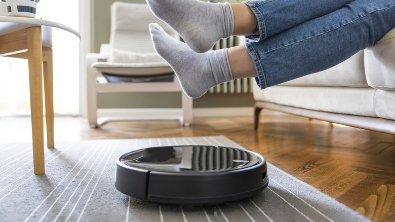 A person raising their legs to let a robot vacuum pass on the floor