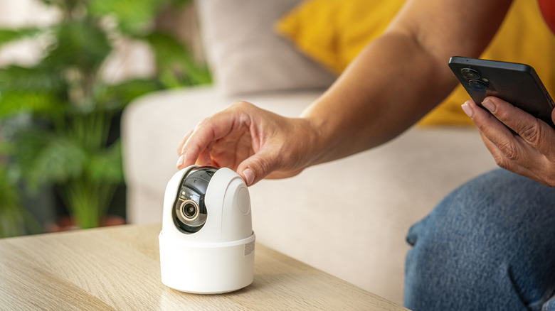 A person setting up a security camera while holding their phone