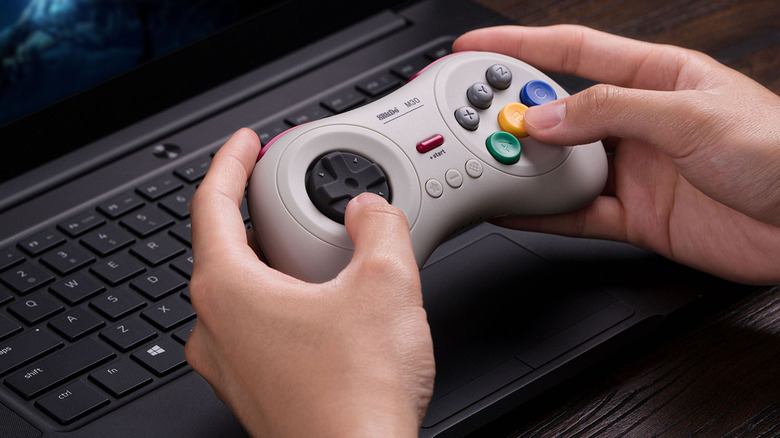 A person using the 8BitDo M30 controller to play a game on their laptop