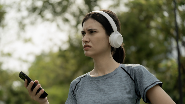 A woman looking confused at her smartphone, while she wears headphones.