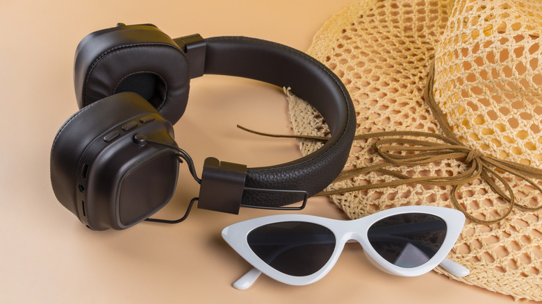 A pair of clean, new-looking headphones next to some sunglasses and a hat.