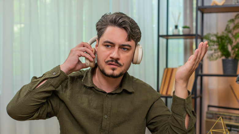 A frustrated-looking man removing a pair of headphones.