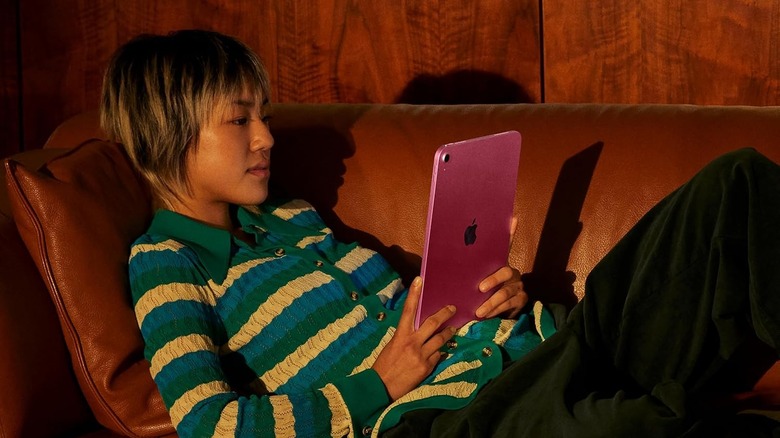 A person using the Apple iPad (A16) tablet while lying on a couch.