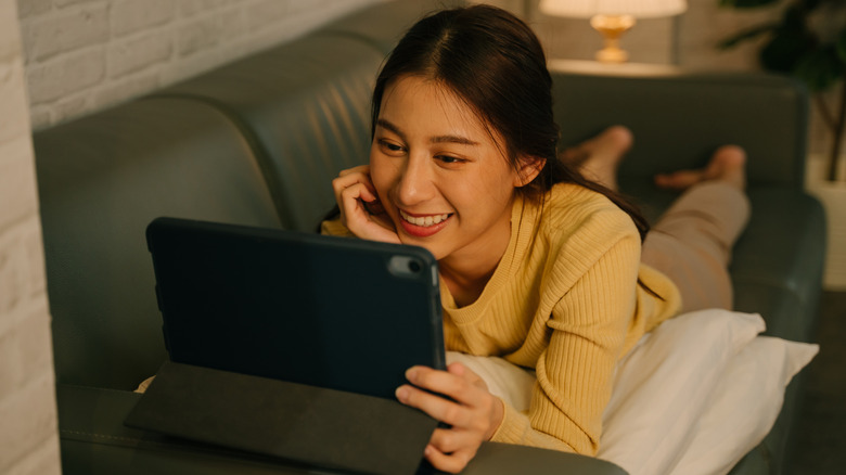 A woman looking at a tablet screen while lying on a couch.