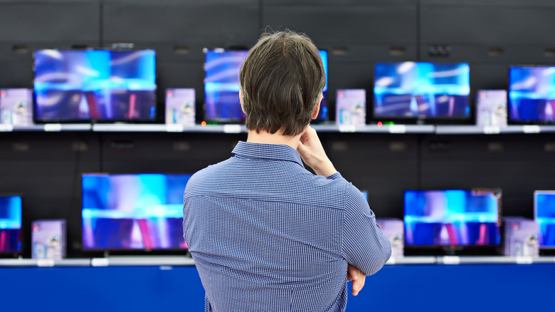A man looking at a wall of TVs.