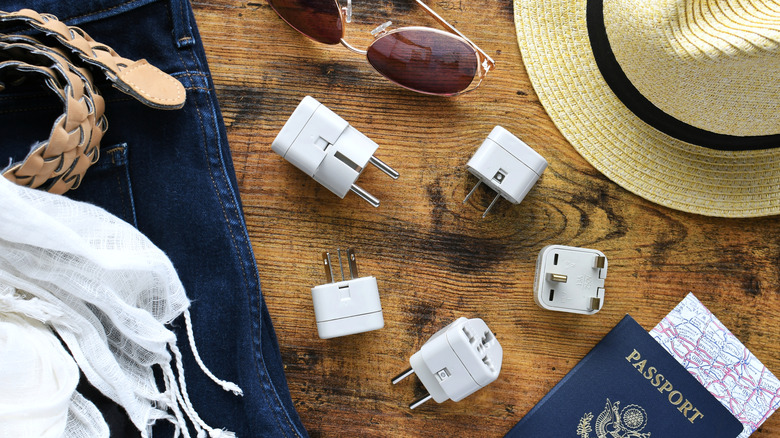 Travel adapters with other travel essentials on a desk.