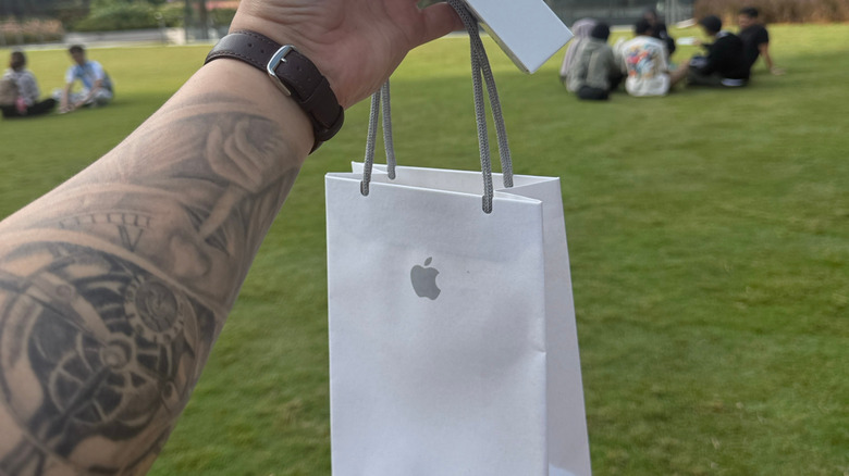A person with an arm tattoo holds an Apple bag with iPhone box