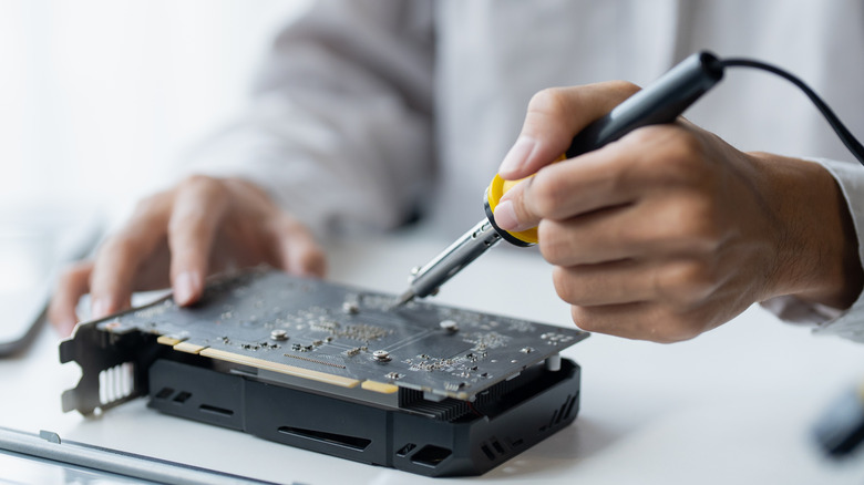 A person repairing a GPU with a soldering iron.
