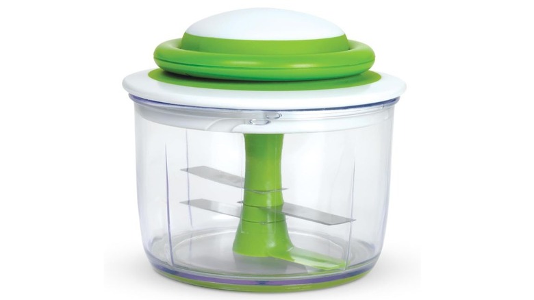 A transparent bowl with a white and green cap. There is a green cylinder inside the bowl with three rectangular blades attached