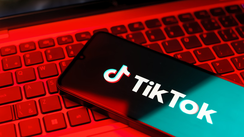 A phone displaying the TikTok logo and label lying on top of a laptop keyboard under a red light