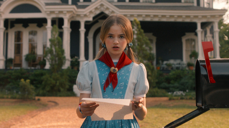 Holly looking at a letter in front of the Creel House in Stranger Things.