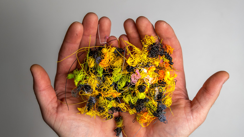 A pair of hands holding thin filament waste in various colors
