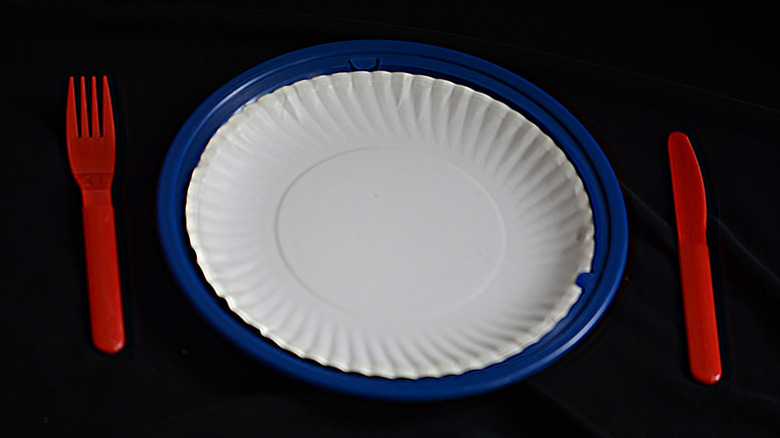 A white paper plate in a blue plastic holder flanked by a red plastic knife and fork on either side