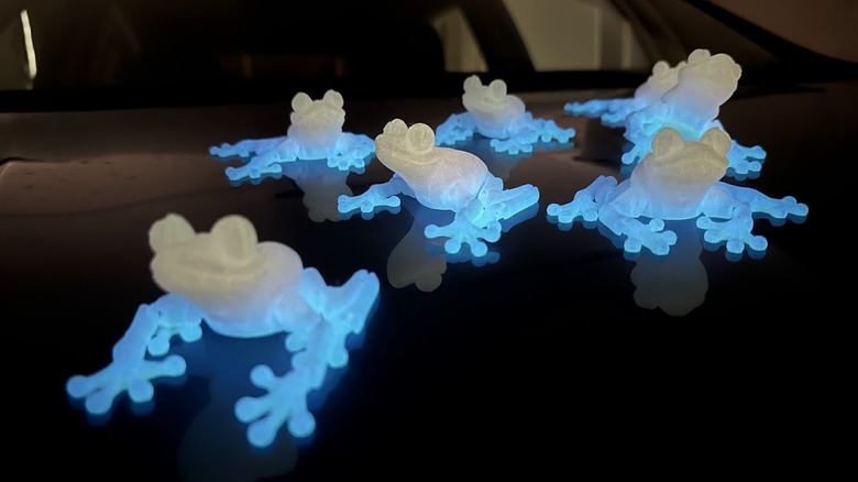 Glow-in-the-dark 3D-printed frogs glowing neon blue at the bases