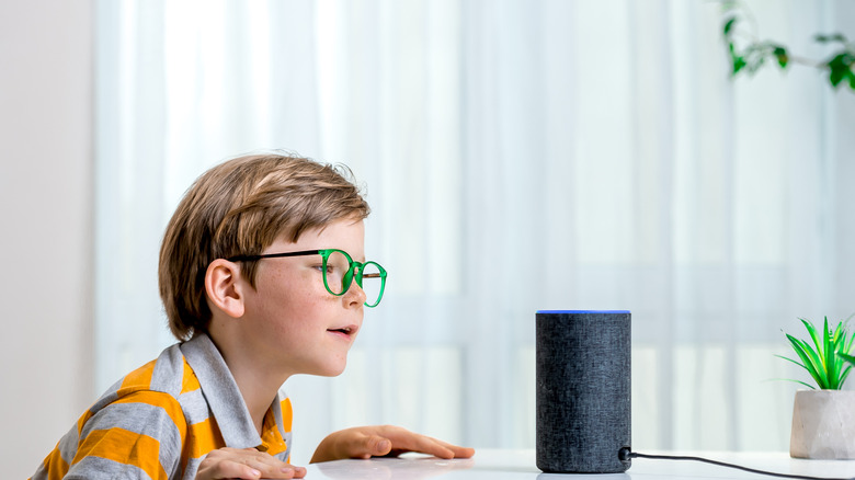 A bespectacled kid talking to their Amazon Echo speaker at home