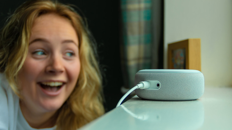 A person smiling and laughing while talking to an Amazon Echo Dot