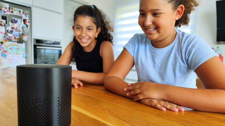 Two kids looking at a speaker on a wooden table and smiling