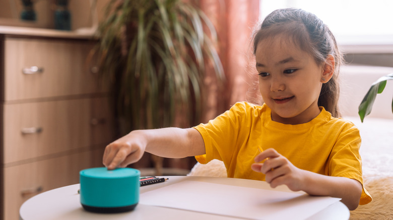 A child sitting on the table as they interact with an Alexa speaker