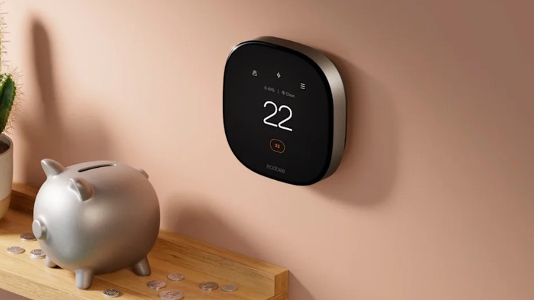 An Ecobee Smart Thermostat Premium installed on the wall, with a table underneath it showing a piggy bank on top.