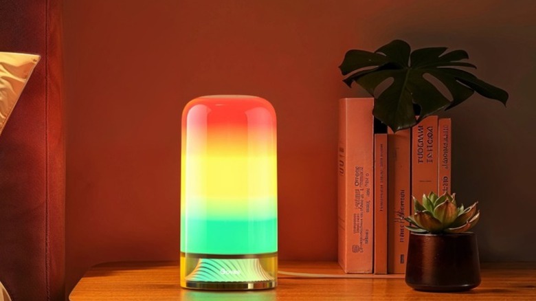 A Govee Smart Table Lamp 2 sat on a bedside table, next to a plant and some books.