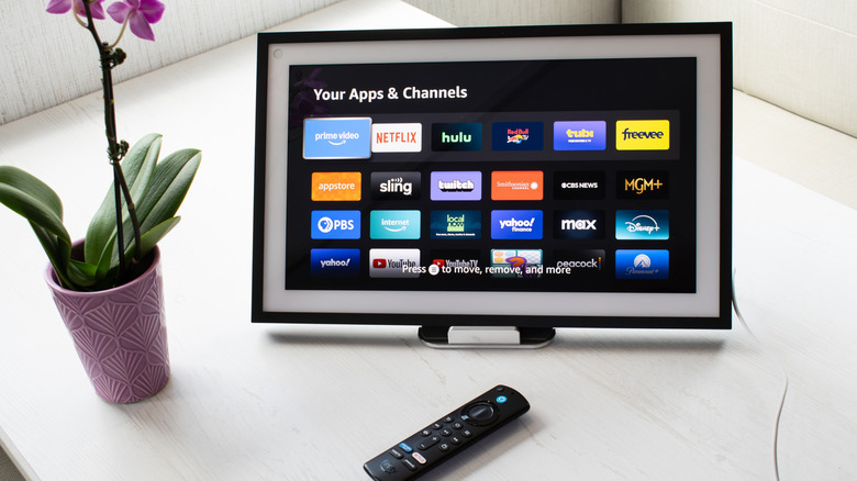 An Amazon Echo Show positioned on a table with a Fire TV remote and a plant next to it.