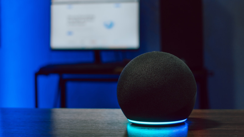 An Amazon Echo Dot sat on top of a table, with a monitor in the background.