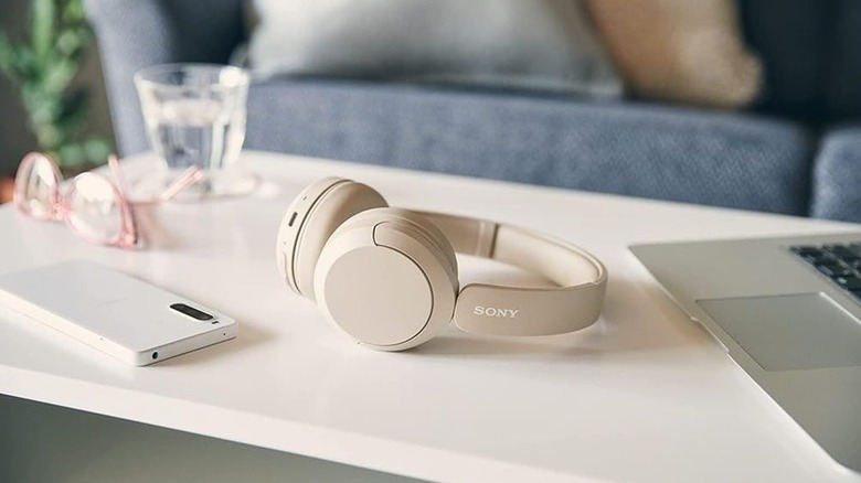 Sony wireless headphones placed beside a laptop and a smartphone.