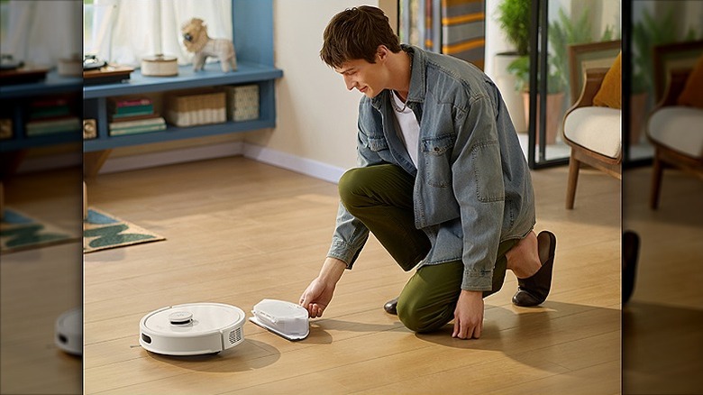 Man using a robot vacuum on a wooden floor.