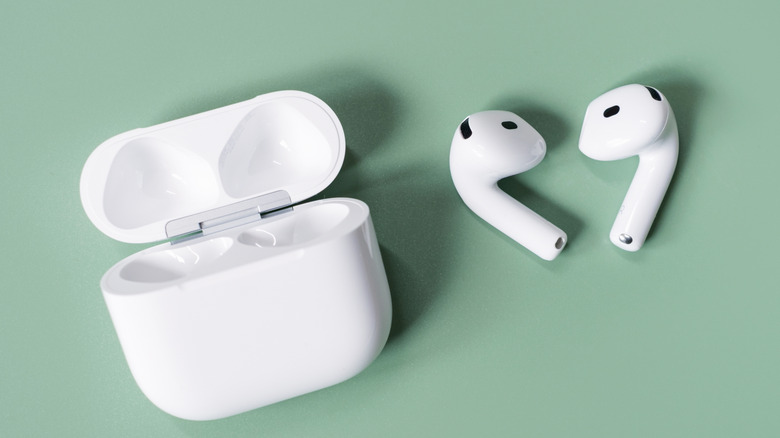 The Apple AirPods 4 wireless earbuds with their charging case on a green surface.