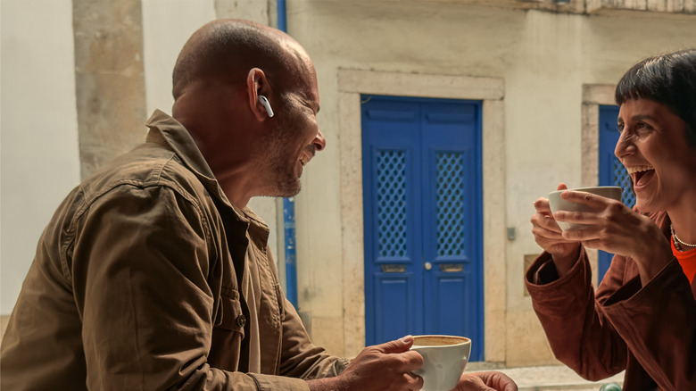 Two people sitting at a cafe table, and one wearing AirPods while talking