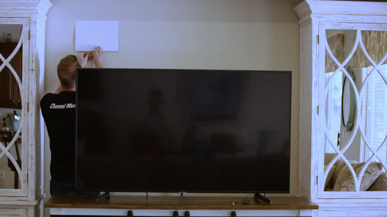 An installer putting a FLATenna on a wall behind a television.