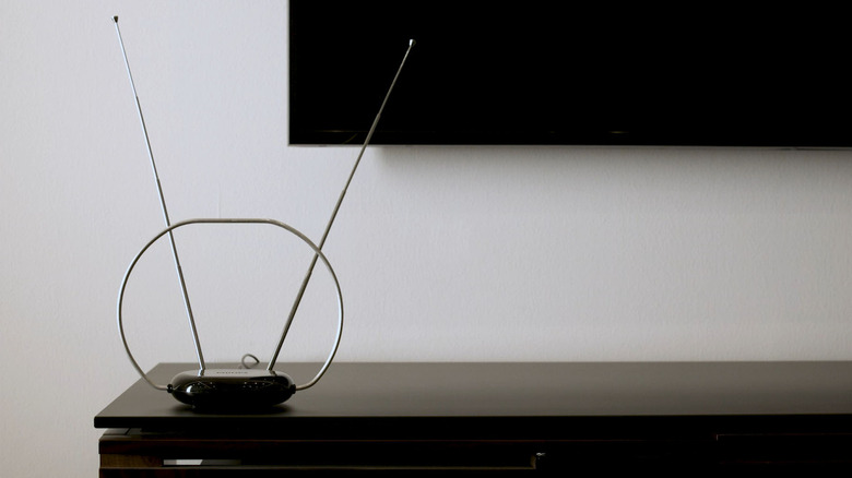 A Philips Rabbit Ears antenna on an entertainment stand near a flat screen TV.