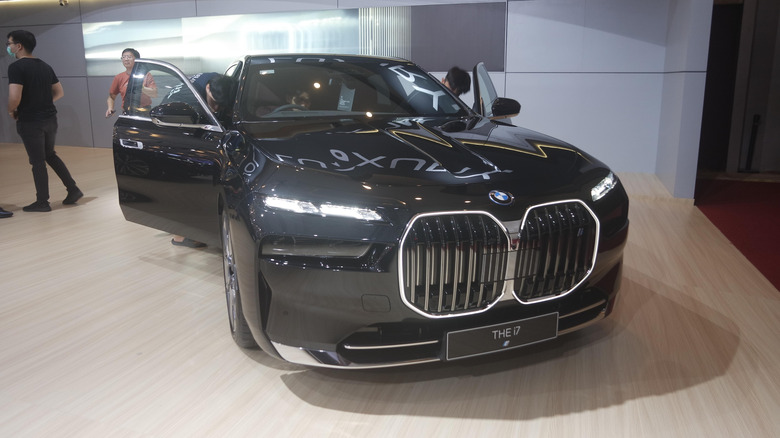 A front view of a black BMW i7 luxury sedan with its doors open as people inspect the car.