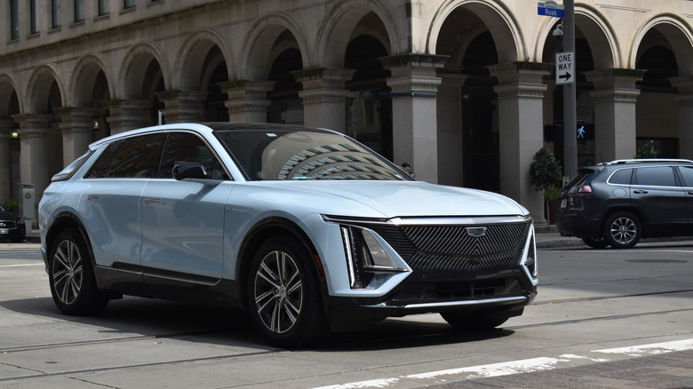A light blue Cadillac electric SUV on a street lined with large stone archways.