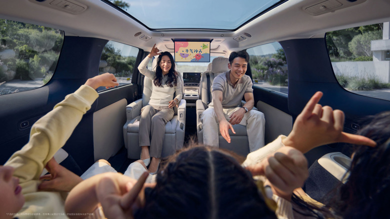 Two smiling adults and three children sitting inside a luxury vehicle with a panoramic sunroof.