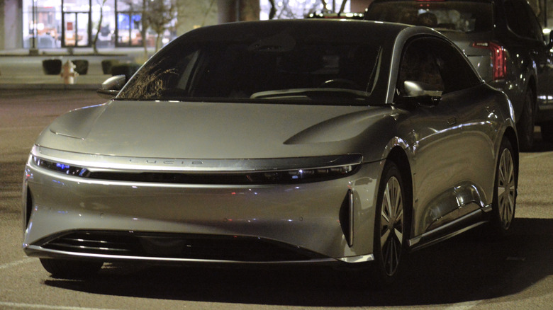 A silver Lucid electric sedan parked on a city street at night.