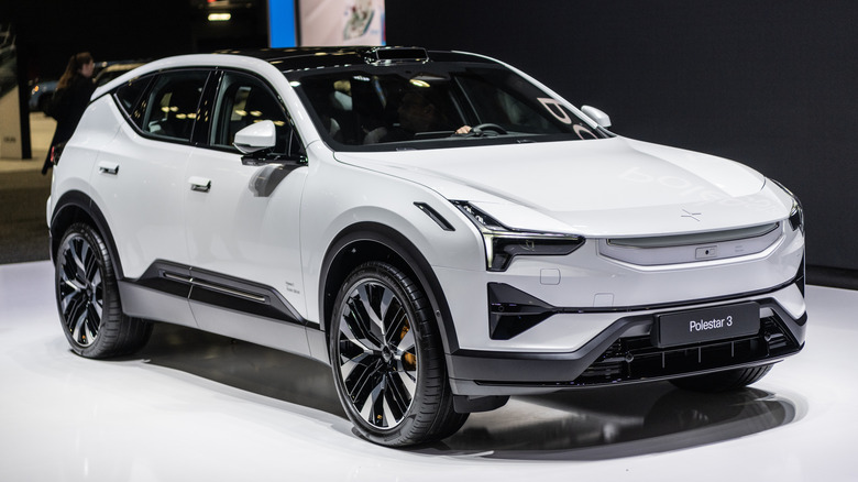 A white Polestar 3 electric SUV displayed indoors on a show floor under bright exhibition lighting.