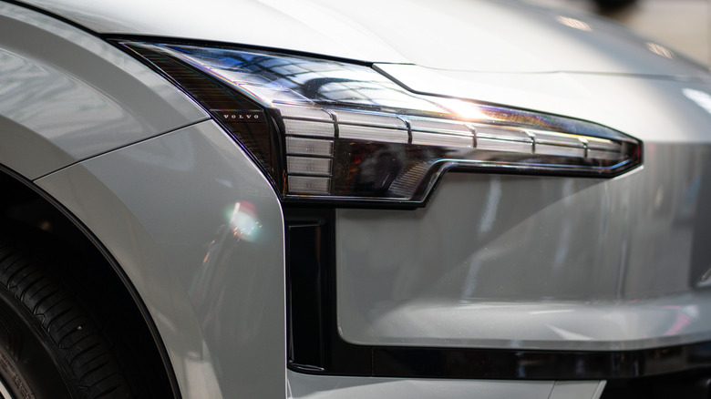 A close-up of the front headlight and fender of a glossy white Volvo.