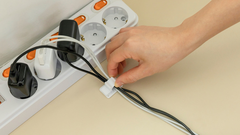A person using cable clips to organize the wires of chargers plugged into a power strip.