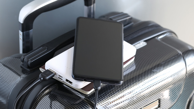 A phone connected to a power bank sitting on top of a suitcase