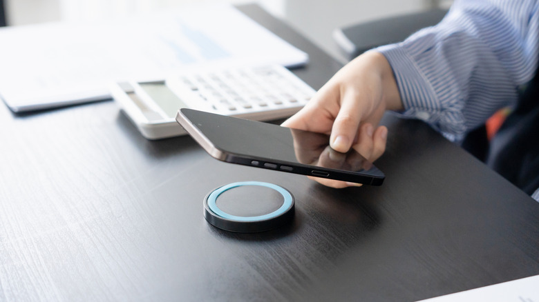 A person holding their phone up above a wireless charging stand