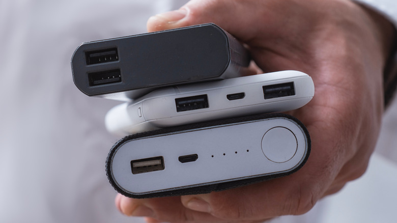 Closeup of a person's hand holding three power banks of various thicknesses and styles