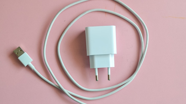 A white charger brick with a detached USB cable circling it on a pink surface